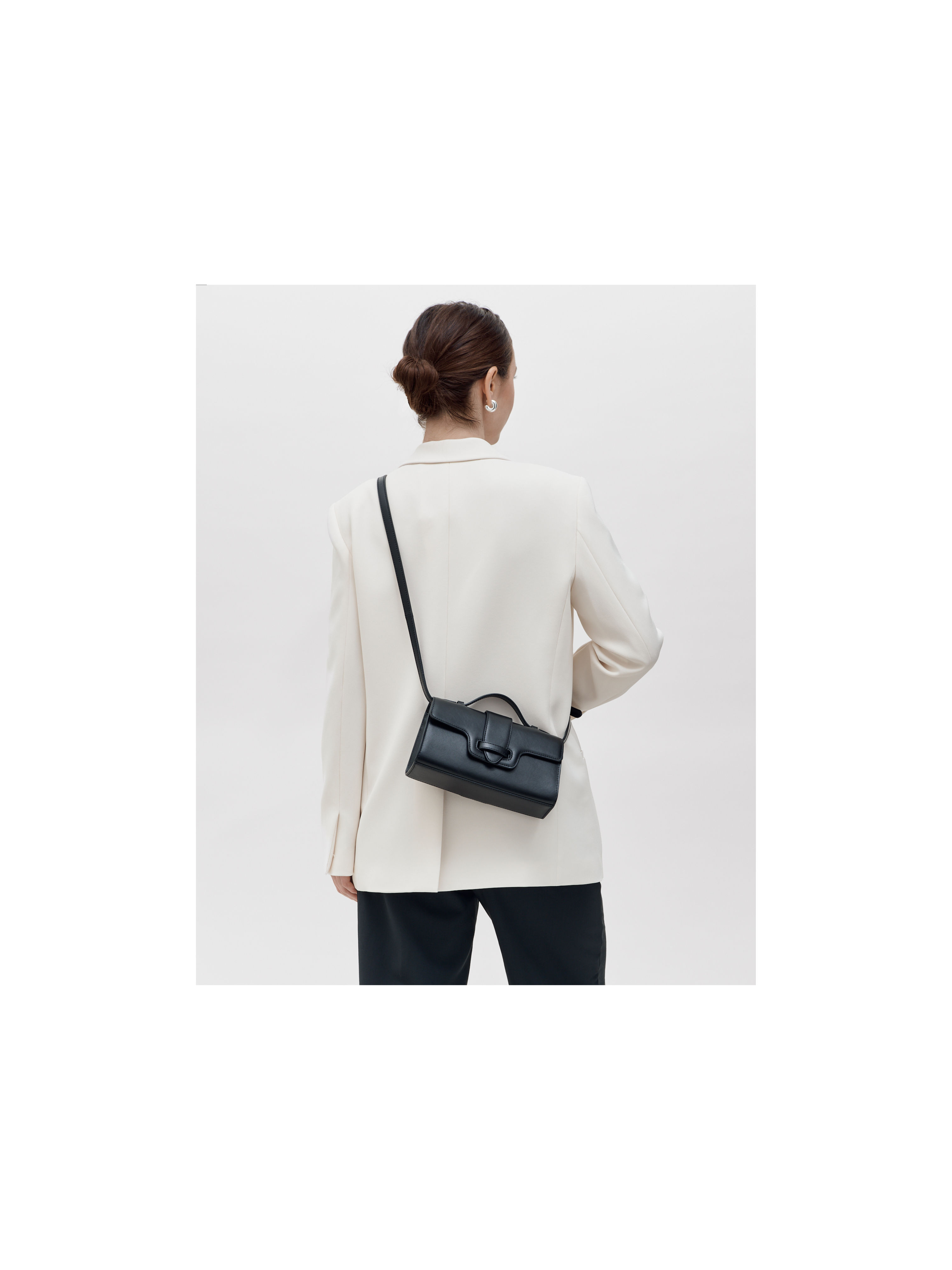 Person wearing a black handbag over one shoulder against a white background | MIRUM bag luxury vegan bags best sustainable handbags savette pochette symmetry pochette savette pochette kelly pochette top handle bag 2025 it bags Stella mccartney ryderbag themoire the moire ethical luxury Spanish handbag brands Spanish bags black mini bag clutch black bag black bags small black bag clutch
