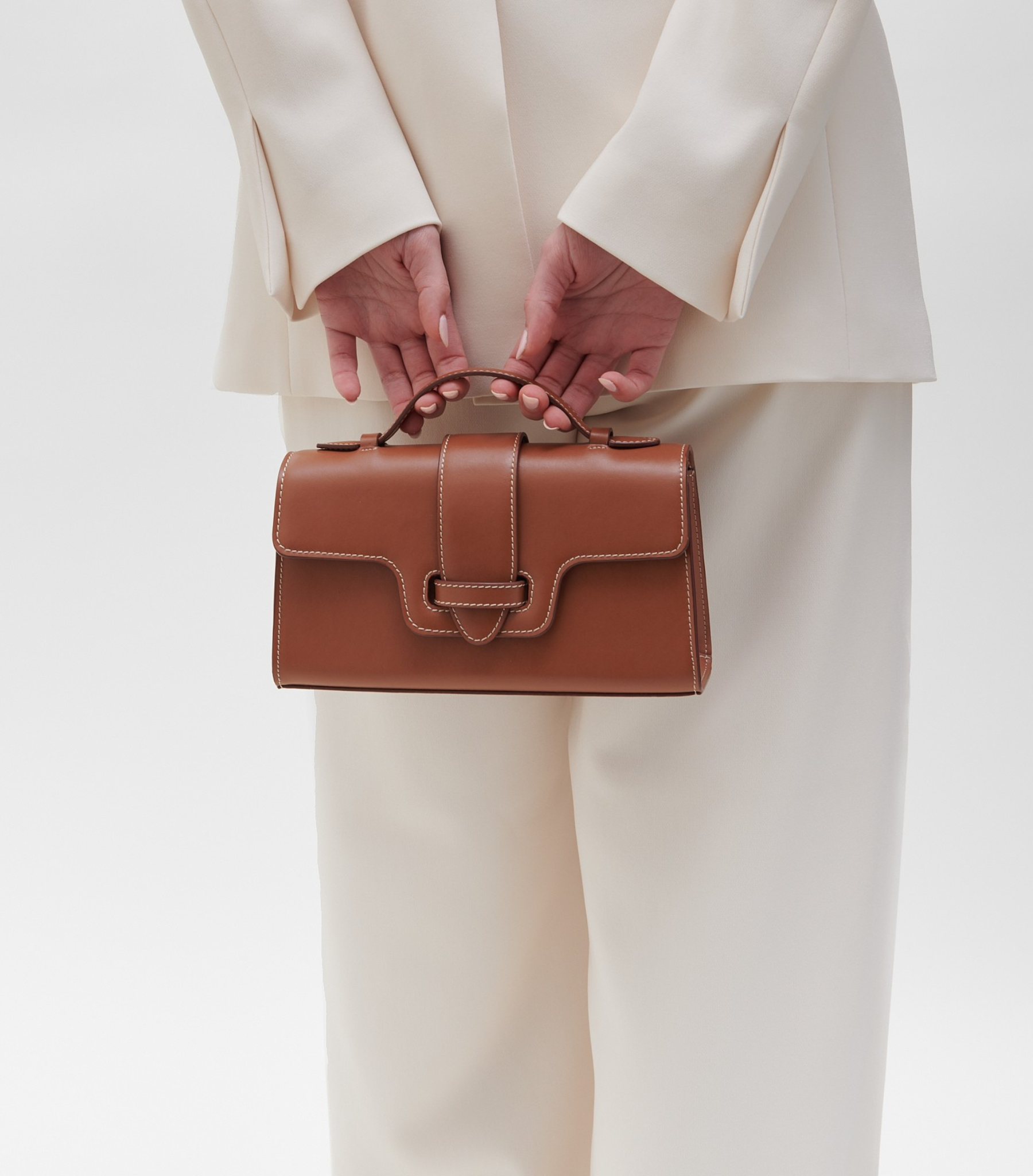 Plant Based Vegan Luxury Sustainable Handbag Made in Spain Ubrique Ethical plant-based leather vegan leather savette symmetry pochette clutch top handle cognac tan brown contrast stitching brown small bag chic classy vegan luxury bags ethical luxury quiet luxury plastic-free leather best british handbag brands mid range handbags 