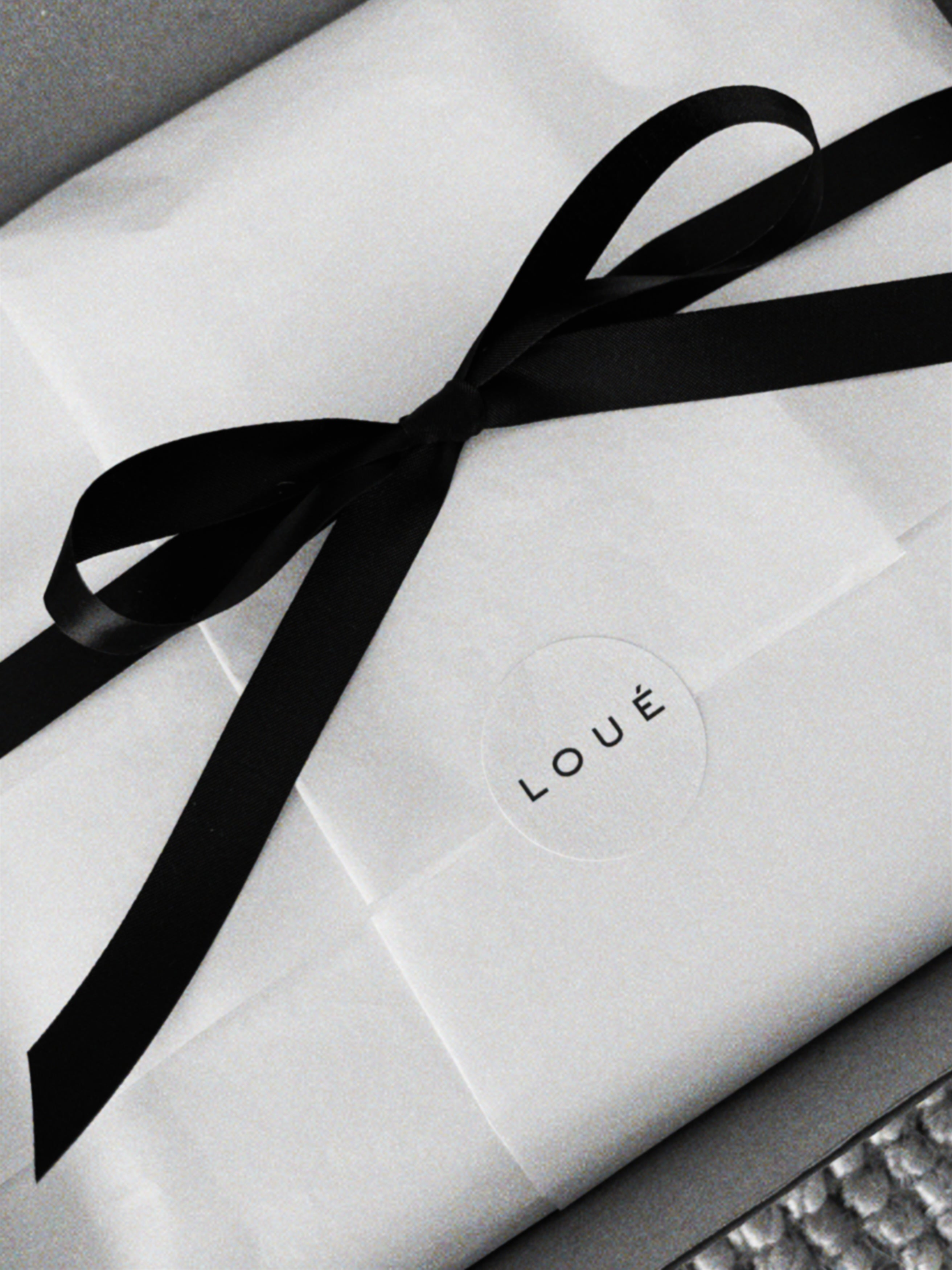 White tissue paper gift wrapping tied with a wide black ribbon bow and sealed with a circular sticker that reads 'LOVE'.